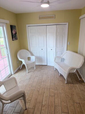 Ein Zimmer mit Holzboden, weißen Korbsesseln, einer weißen Tür mit dem Schriftzug 'WELCOME' und einem Deckenventilator.