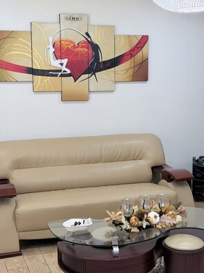A living room with a beige sofa, a glass coffee table with decorative items, and a large abstract painting on the wall. - Cozy 2-bedroom house in fabulous in Pocono Mountain (Tobyhanna)