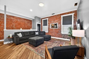 Ein modernes Wohnzimmer mit Ecksofa, Pouf und einem gemusterten Teppich.