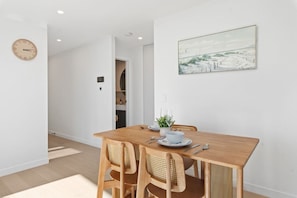 A dining area with a wooden table, four chairs, a clock, and a painting on the wall. - Elegant 2BR Broadbeach Island Getaway (Broadbeach)