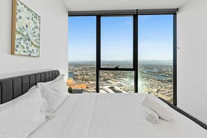 A bedroom with a large bed, a view of a cityscape through floor-to-ceiling windows, and a framed artwork on the wall. - Elegant 2BR Broadbeach Island Getaway (Broadbeach)