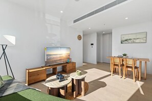 A modern living room with a flat-screen TV, a dining area with a wooden table and chairs, and a green carpet. - Elegant 2BR Broadbeach Island Getaway (Broadbeach)