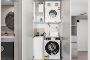 A compact laundry room with a front-loading washing machine, a sink, and a mirror. - Luxury 2BR Broadbeach Island Escape (Broadbeach)
