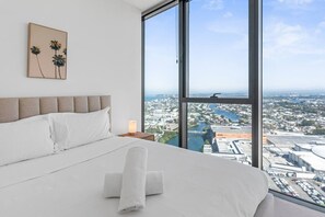 A hotel room with a large bed, a nightstand with a lamp, and a city view through large windows. - Luxury 2BR Broadbeach Island Escape (Broadbeach)