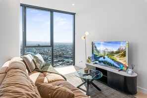 Een moderne woonkamer met een groot raam, een bank, een glazen salontafel en een flatscreen televisie.