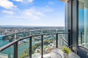 Varanda com guarda-corpo de vidro, vista para a paisagem urbana e um corpo d'água.