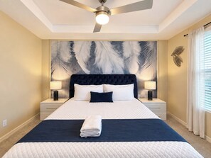 Une chambre d’hôtel avec un grand lit, un ventilateur de plafond et une décoration murale représentant des plumes.