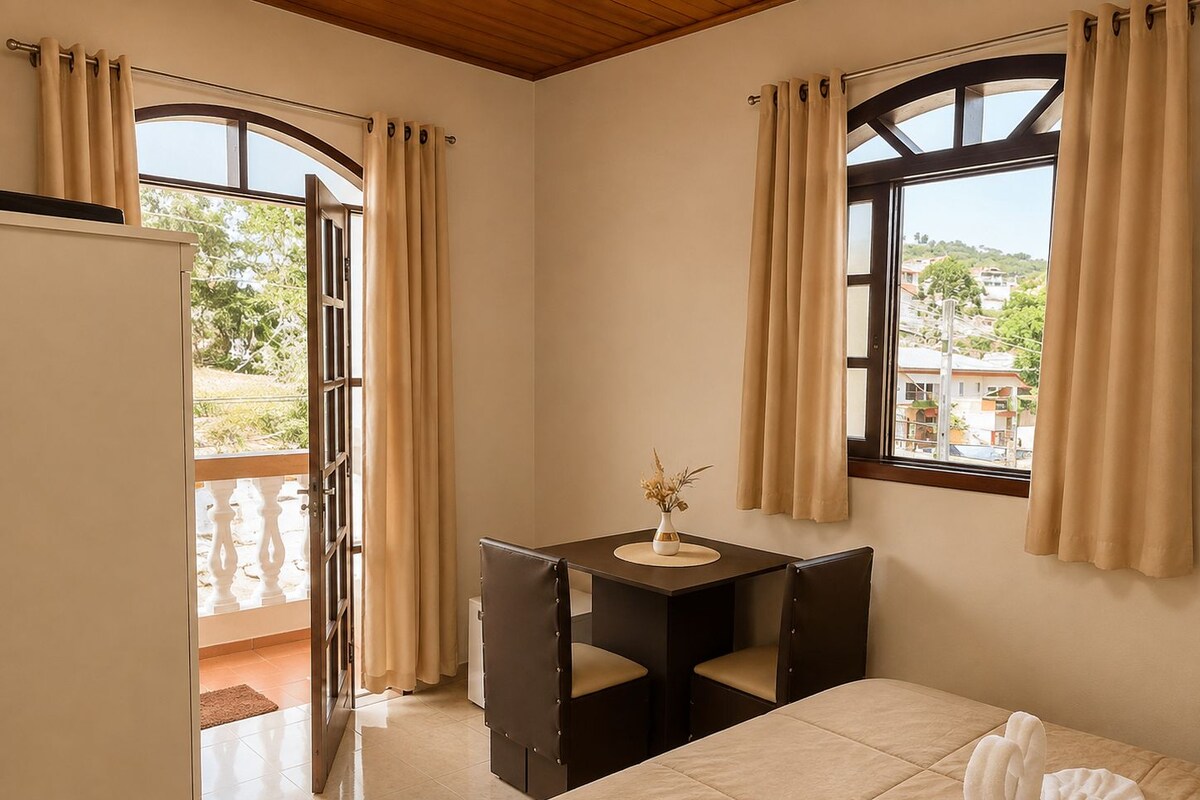 A hotel room with a bed, a desk with a chair, a window with curtains, and a view of the outside.