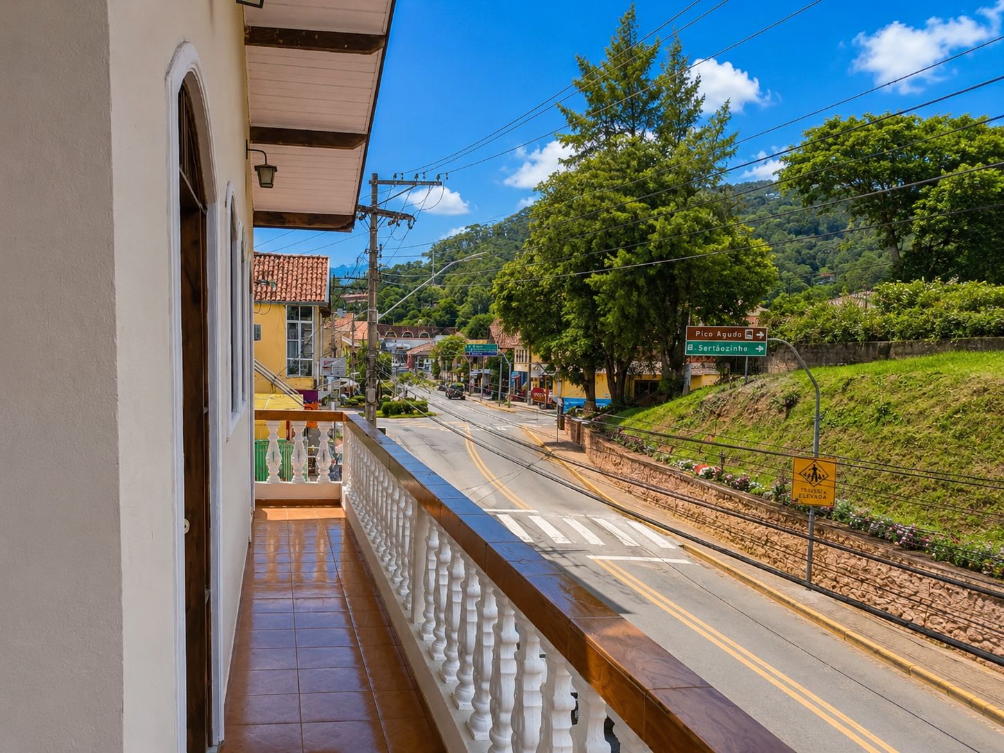 Varanda com vista para uma rua, uma linha de trem e uma paisagem montanhosa.