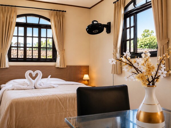 A hotel room with a bed, a table with a vase, and windows with curtains. - Pousada São Benedito  (Santo Antônio do Pinhal)