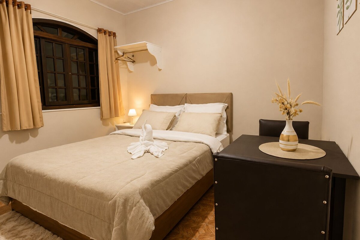 A hotel room with a bed, bedside table, lamp, and a vase with flowers.