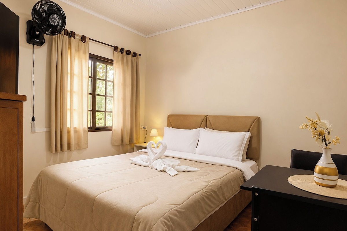 Una habitación de hotel con una cama, una mesita de noche, una lámpara, un ventilador y una ventana con cortinas.