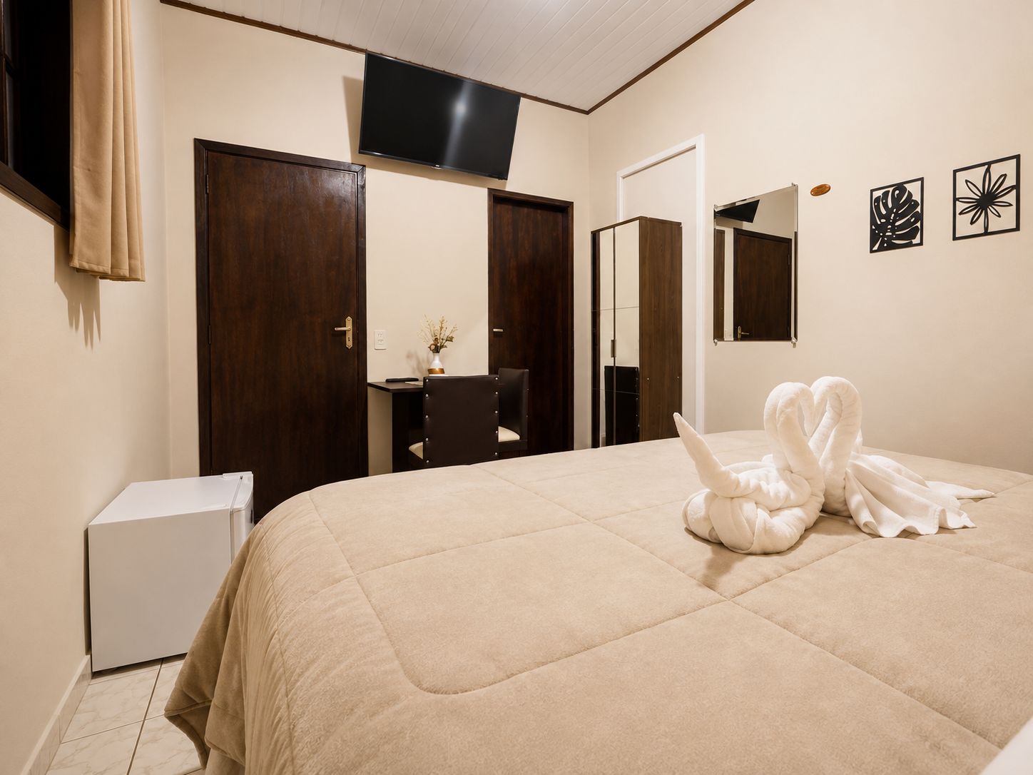 Habitación de hotel con cama, escritorio, silla, televisor y espejo.