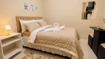 Quarto de hotel com cama, mesa de cabeceira com luminária, tapete macio, escrivaninha com espelho e obras de arte na parede.