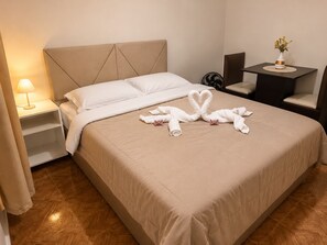 A hotel room with a bed, a nightstand with a lamp, a small table with a vase, and a chair. - Pousada São Benedito  (Santo Antônio do Pinhal)