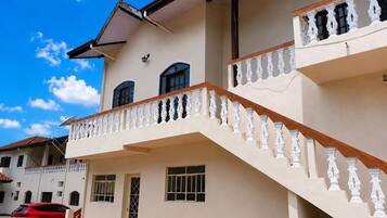 Ein zweistöckiges Gebäude mit weißer Fassade, einem Balkon mit aufwendiger Balustrade und einem roten Auto davor.