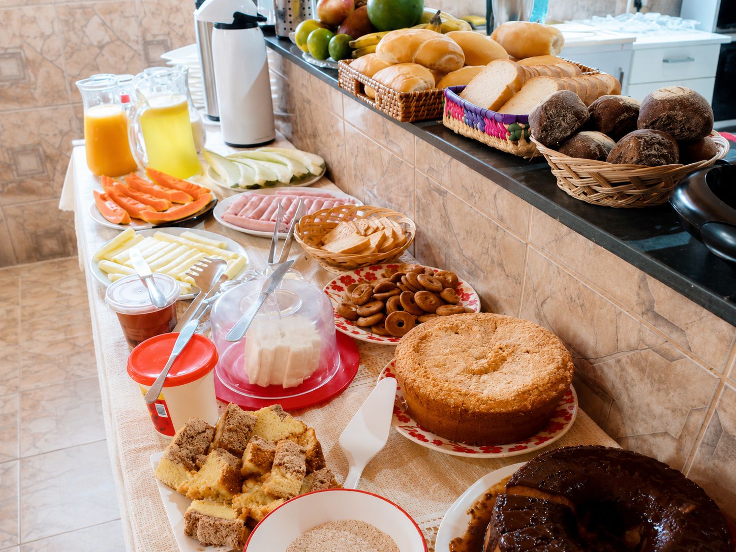 Une table de buffet proposant divers aliments, notamment du pain, des pâtisseries et un gâteau.