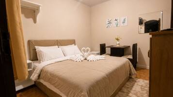 A hotel room with a bed, a bedside table with a vase of flowers, a small table with a fan, and a mirror on the wall.
