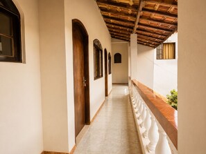 A corridor with a tiled floor, wooden doors, and a balcony with white balustrades. - Pousada São Benedito  (Santo Antônio do Pinhal)