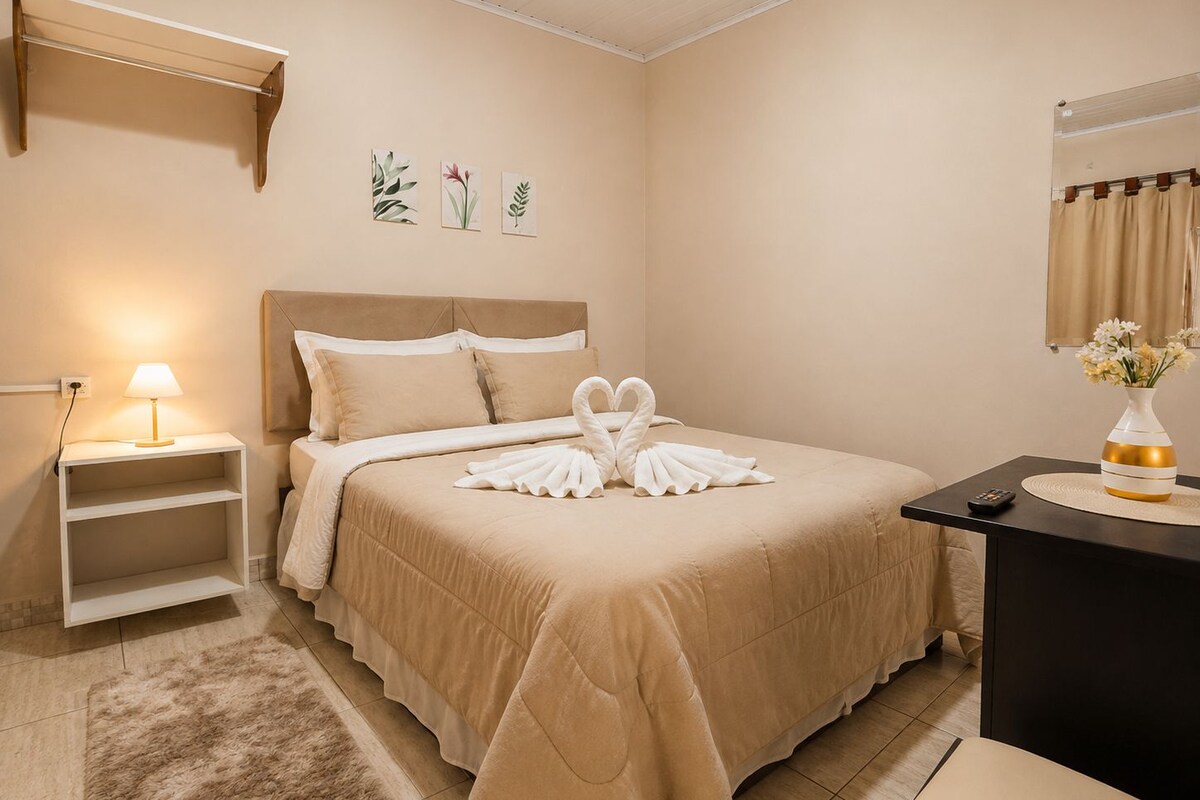 A hotel room with a bed, a nightstand, a lamp, a vase with flowers, and a wall-mounted shelf with plant illustrations.