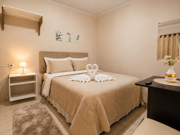 A hotel room with a bed, a nightstand, a lamp, a vase with flowers, and a wall-mounted shelf with plant illustrations.