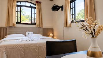 A hotel room with a bed, a table with a vase, and two windows with curtains.
