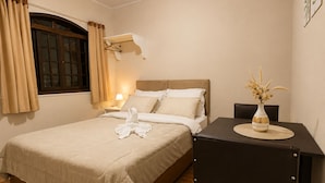 Une chambre d’hôtel avec un lit, une table de chevet, une lampe et un vase de fleurs.