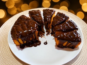 Un postre cubierto de chocolate sobre un plato blanco con un mantel individual texturizado debajo.