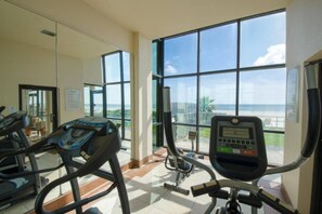 Une salle de sport équipée de tapis de course et d’un vélo d’appartement, avec de grandes fenêtres donnant sur la plage.
