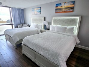 Une chambre d’hôtel avec deux lits, une grande fenêtre avec des rideaux et des œuvres d’art accrochées aux murs.