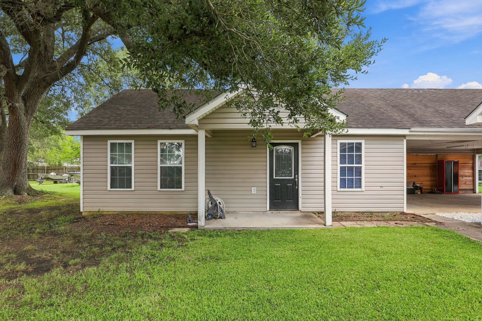 A single-story house with a front porch, a garage, and a tree in the yard.