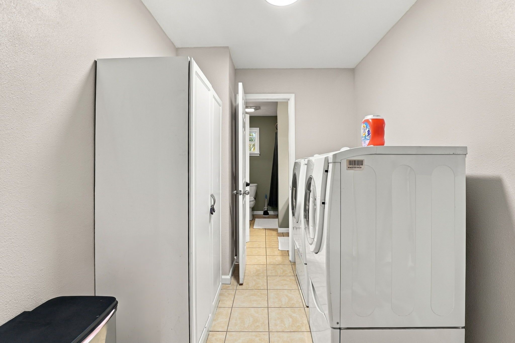 A laundry room with a washing machine, dryer, and a trash bin.