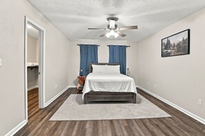 A bedroom with a bed, a ceiling fan, a painting, and a view into another room. - Cozy Mid-City 1BR Home Near Casinos (Lake Charles)