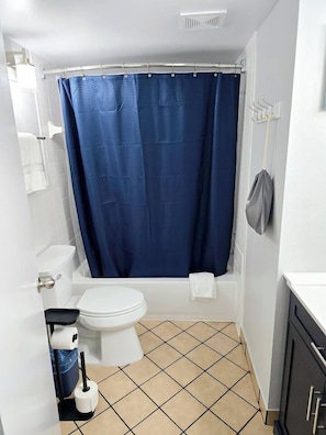 Un baño con inodoro blanco, bañera y cortina de ducha azul.