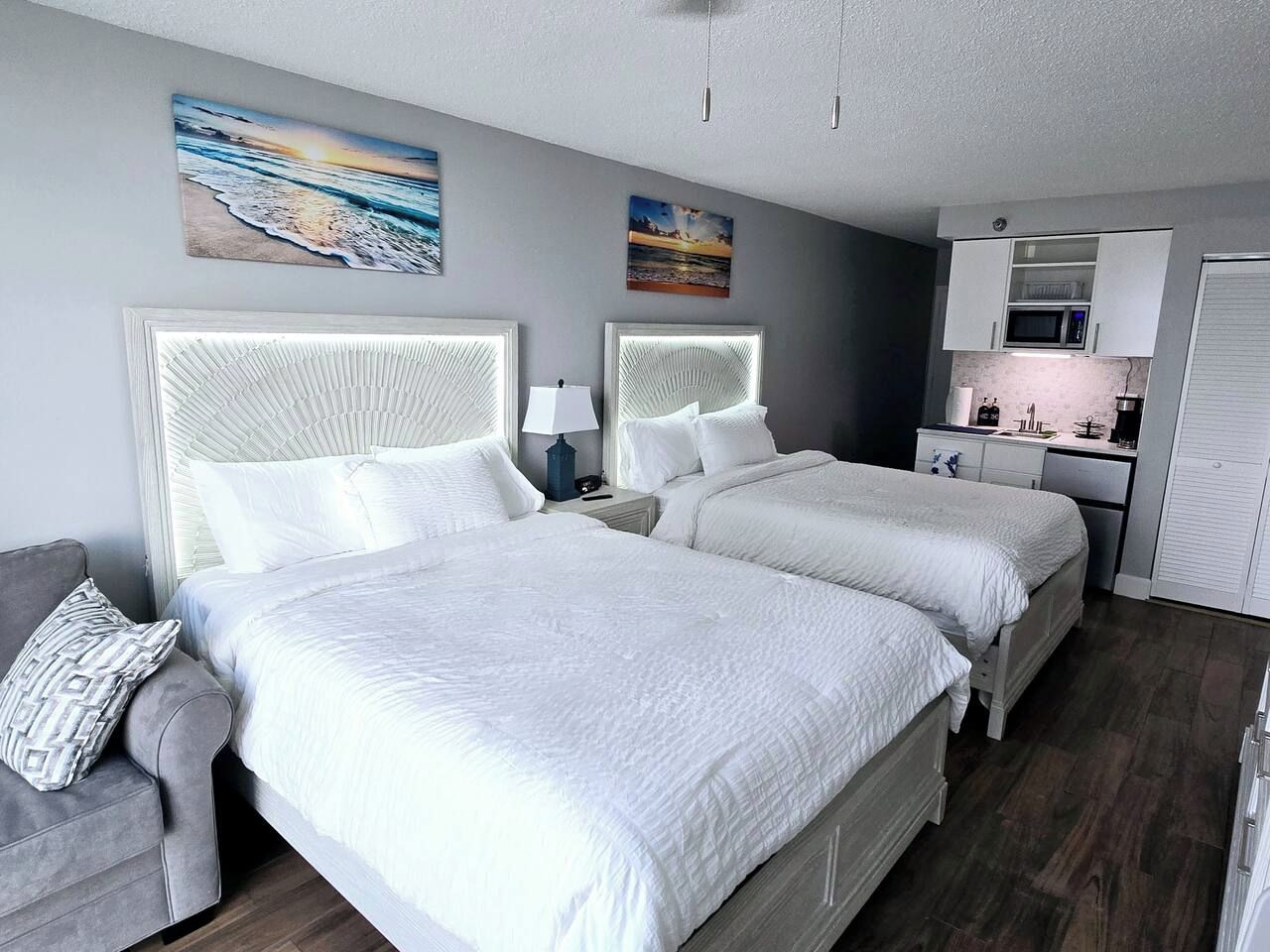 Habitación de hotel con dos camas, kitchenette y obras de arte en las paredes.