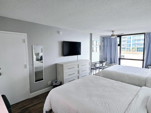 Habitación de hotel con dos camas, una televisión de pantalla plana, un escritorio y una ventana con cortinas.