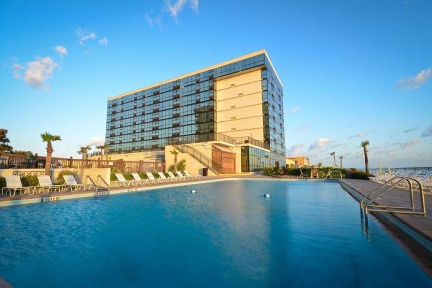 Un hotel moderno con una piscina grande y sillones de sol.