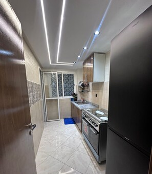 A modern kitchen with a built-in oven, a refrigerator, and a window with a view. - 5 min to Mohammed VI Hospital + 15 min to the airport (Bouskoura)