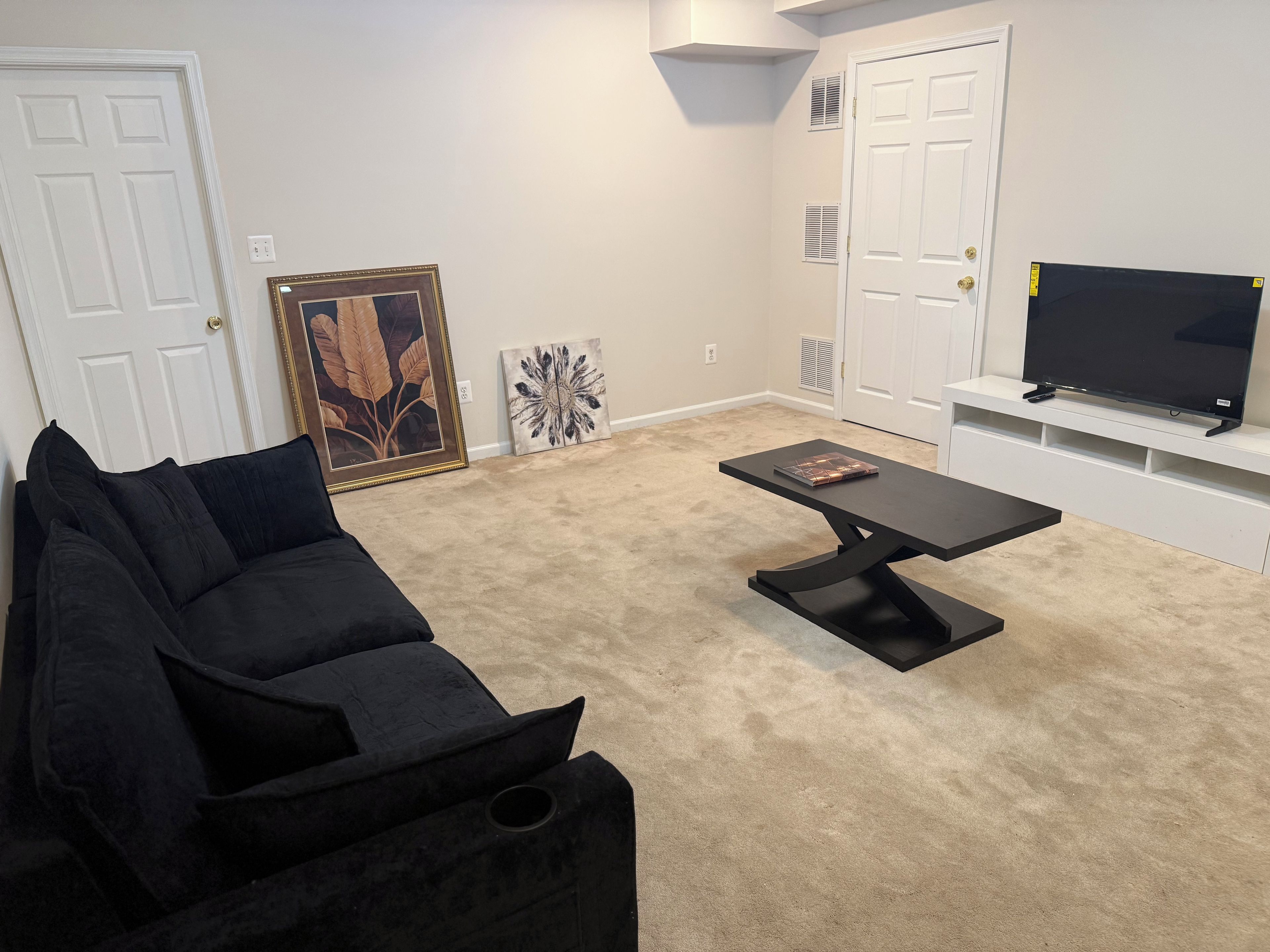 Sala de estar com sofá preto, mesa de centro, TV de tela plana em um suporte branco e obras de arte emolduradas na parede.