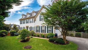 Ett tvåvåningshus med en välskött gräsmatta och en mängd olika buskar och träd.