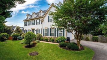 A two-story house with a well-maintained lawn and a variety of shrubs and trees.
