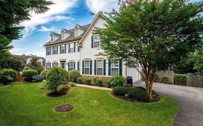 A two-story house with a well-maintained lawn and a variety of shrubs and trees. - Fantastic 2-bedroom apartment in charming Woodbridge (Woodbridge)