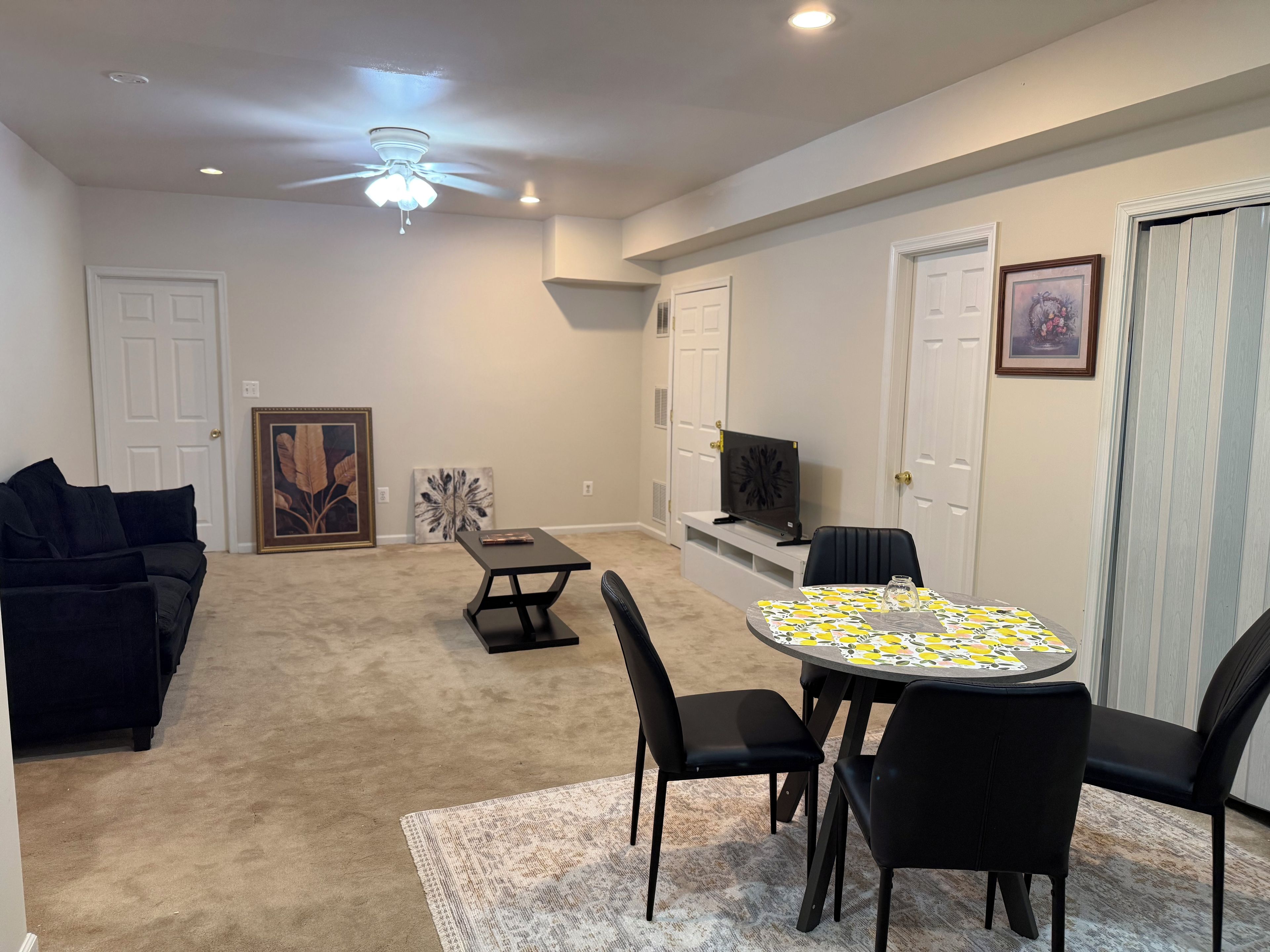 A living room with a sofa, a coffee table, a dining table with chairs, a ceiling fan, and a television on a stand.