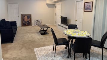 A living room with a sofa, a coffee table, a dining table with chairs, a ceiling fan, and a television on a stand.