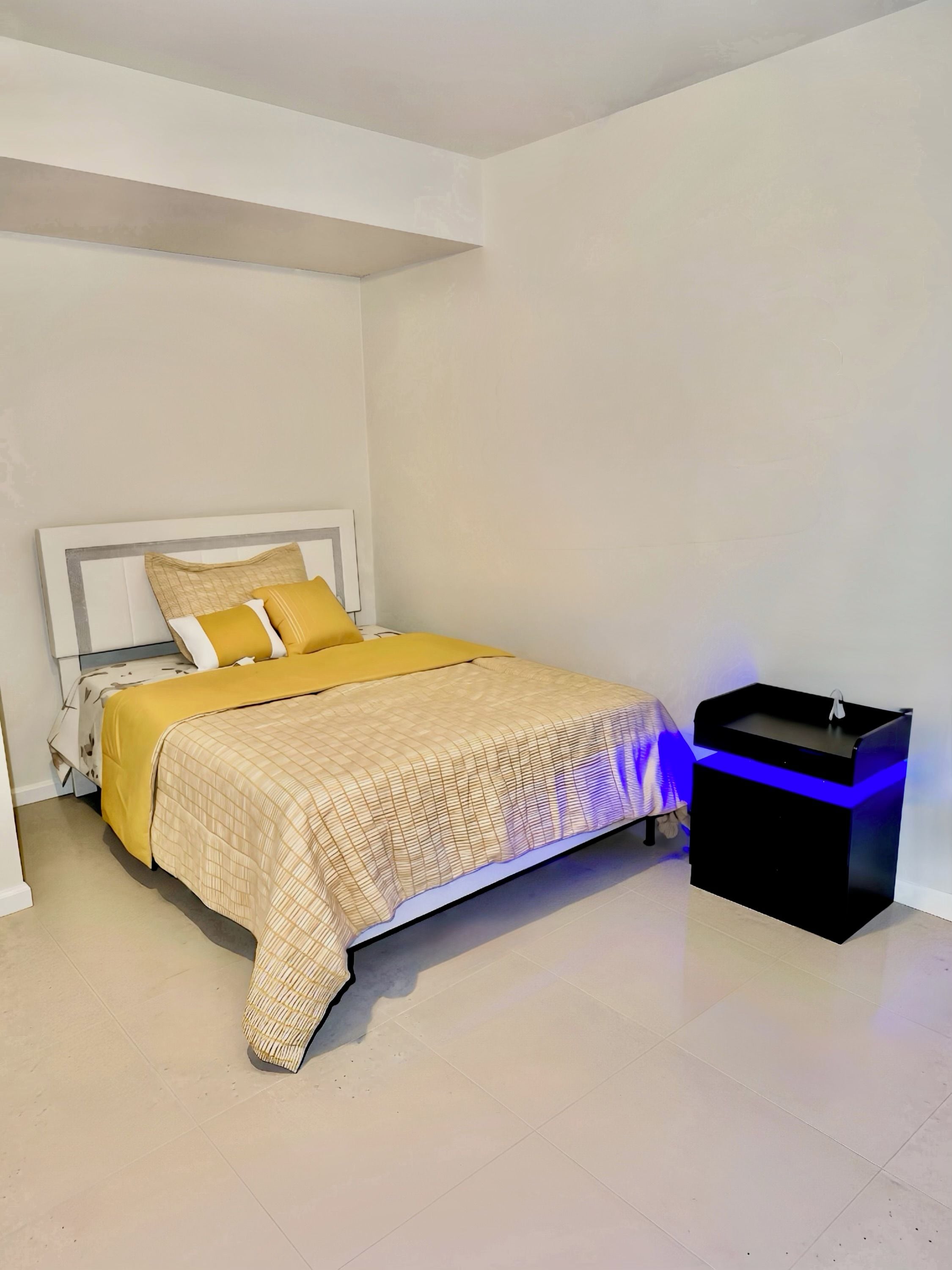 A bedroom with a bed, bedside table, and a nightstand with a sink.