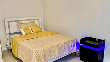 A bedroom with a bed, bedside table, and a nightstand with a sink.
