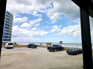 A parking area with vehicles, a building with multiple floors, and a view of the ocean. - Spectacular New King Studio w/kitchenette, pool (Daytona Beach)