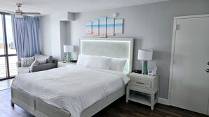 Une chambre à coucher avec un grand lit, une table de chevet avec une lampe, une chaise, une fenêtre avec des rideaux et une porte.