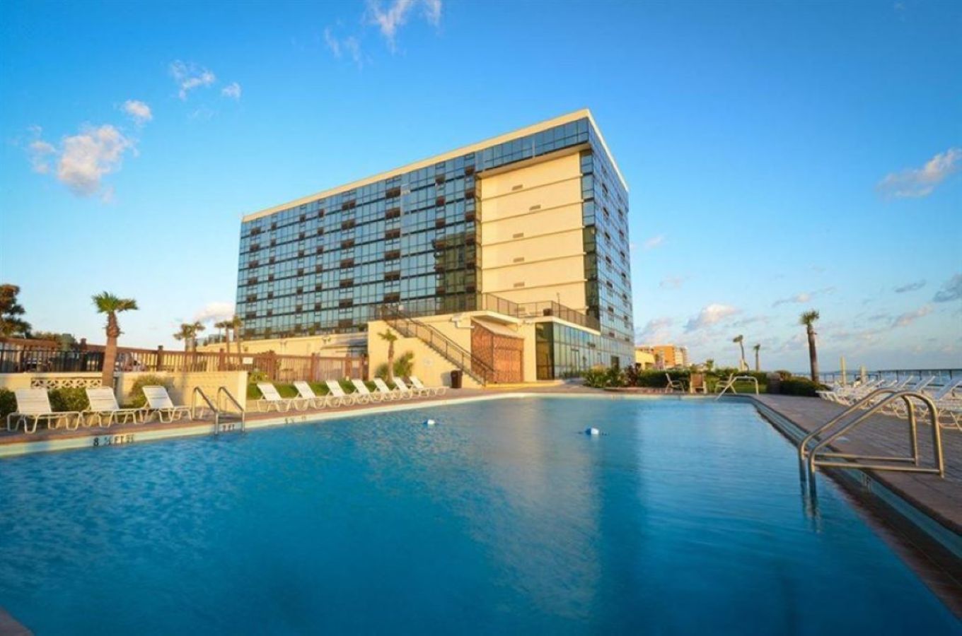 Un hotel moderno con una piscina amplia, tumbonas y vista despejada al océano.