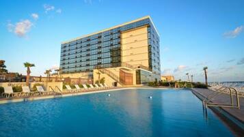 Un hotel moderno con una piscina amplia, tumbonas y vista despejada al océano.